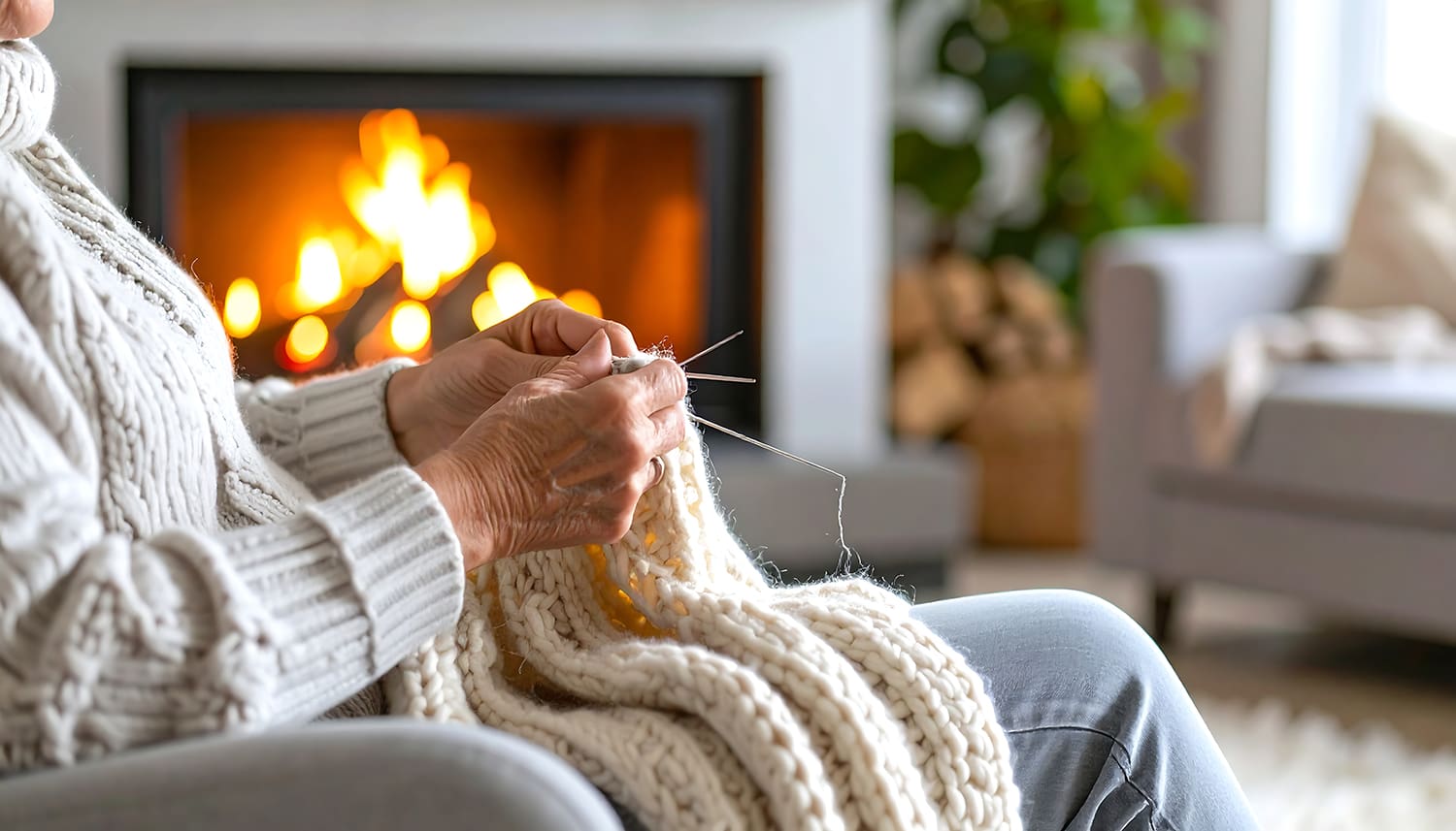 an elderly woman knitting a scarf near a fireplace